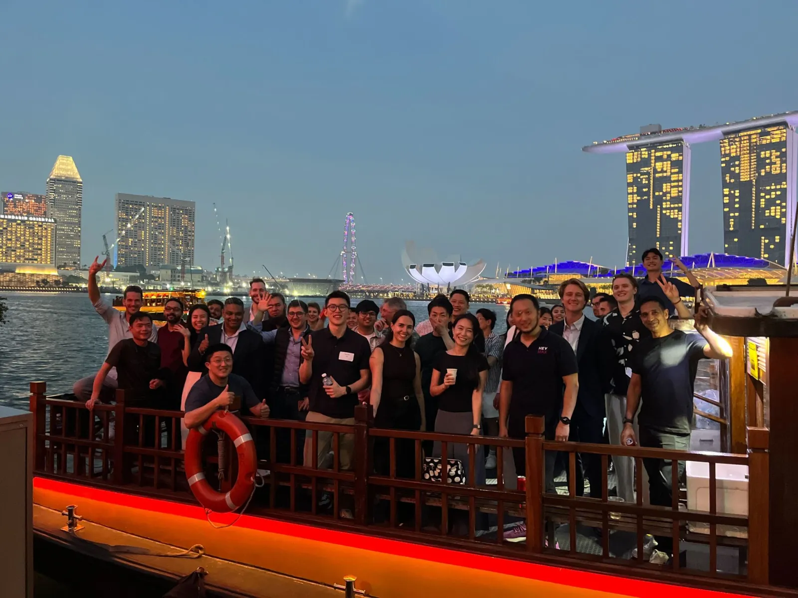 The team and airline guests on a boat in front of the Marina Bay skyline at night